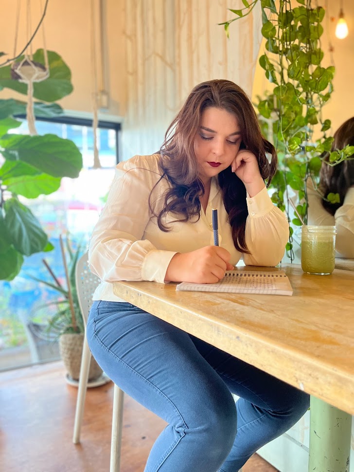 Author Cathrine Swift writes at a butcher block table with lots of greenery around her.